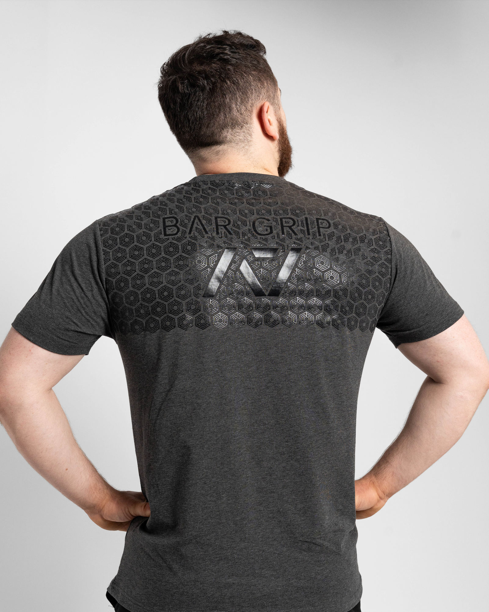 Man wearing a dark gray t-shirt with a7 bar grip on the back against a light gray background