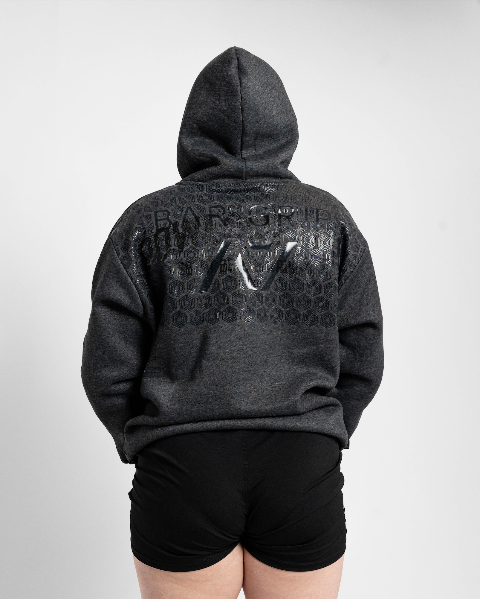 Person wearing a dark gray hoodie with branding on the back against a light gray background