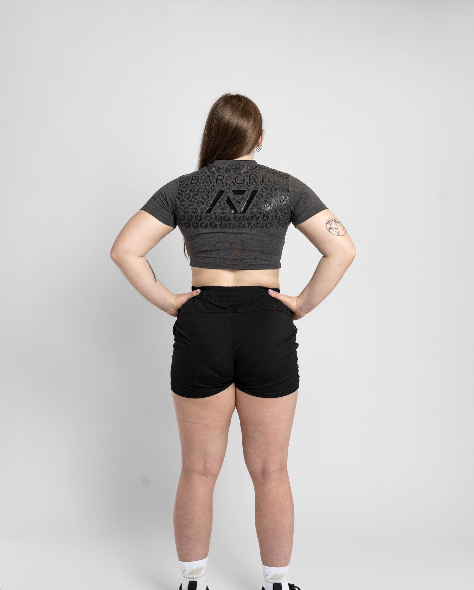 Person wearing a dark gray crop top and black shorts on a light gray background