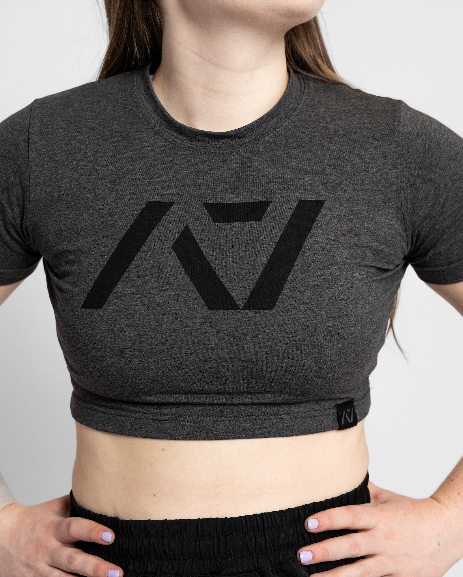 Person wearing a dark gray crop top with a logo on a plain background