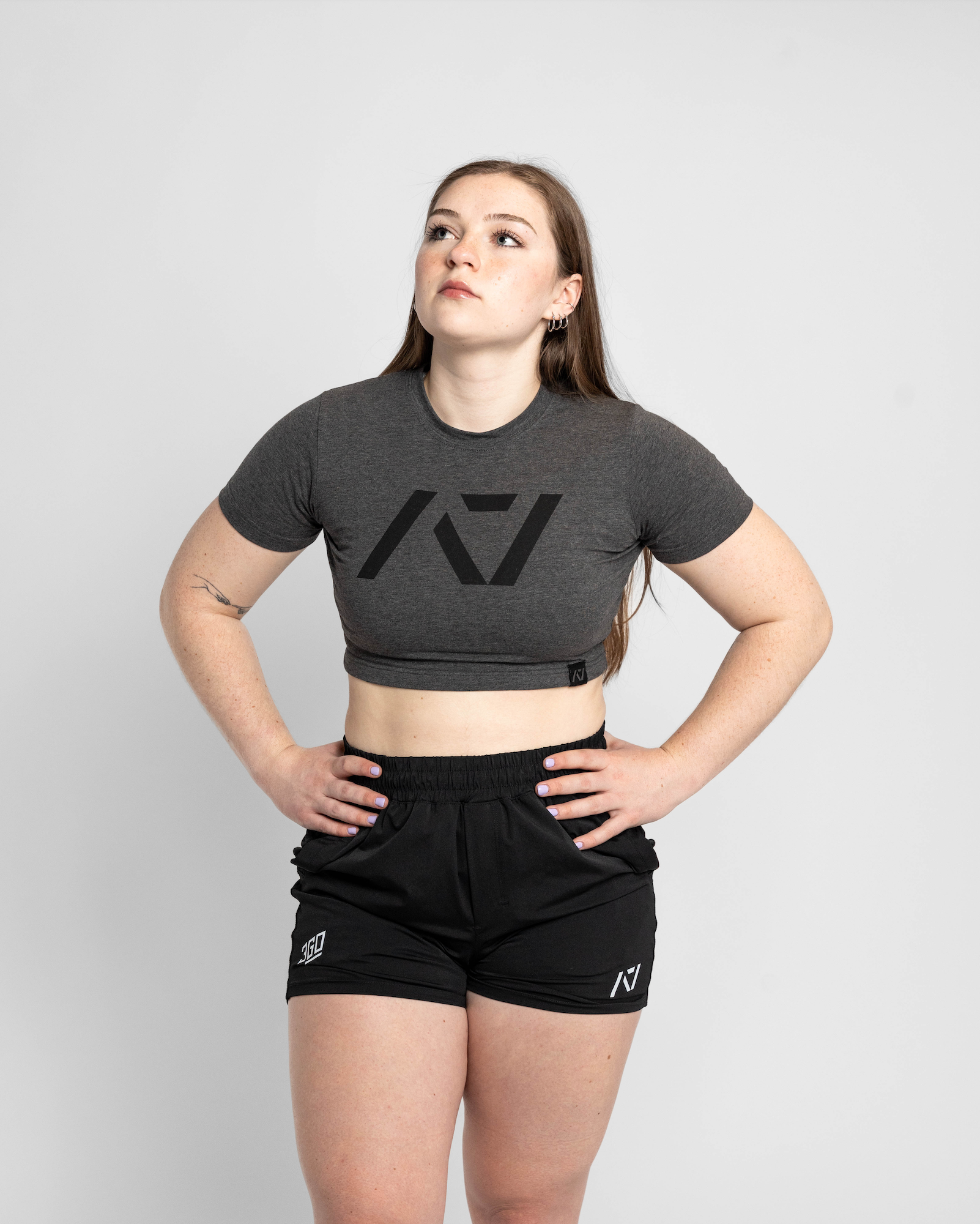 Person wearing a gray crop top with a logo and black shorts on a light gray background